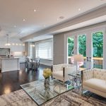 Open-concept living area with white tufted armchairs, French doors to the deck and a white kitchen island beyond