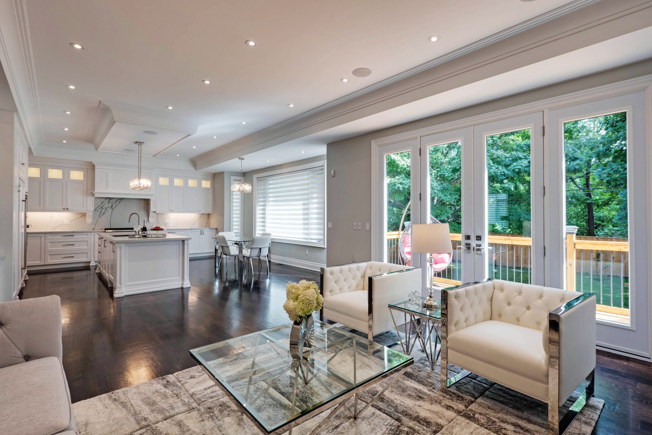 Open-concept living area with white tufted armchairs, French doors to the deck and a white kitchen island beyond