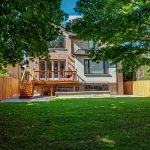 Rear of a two-storey brick home with a new elevated cedar-toned deck, fresh sod, and wood privacy fence on both sides