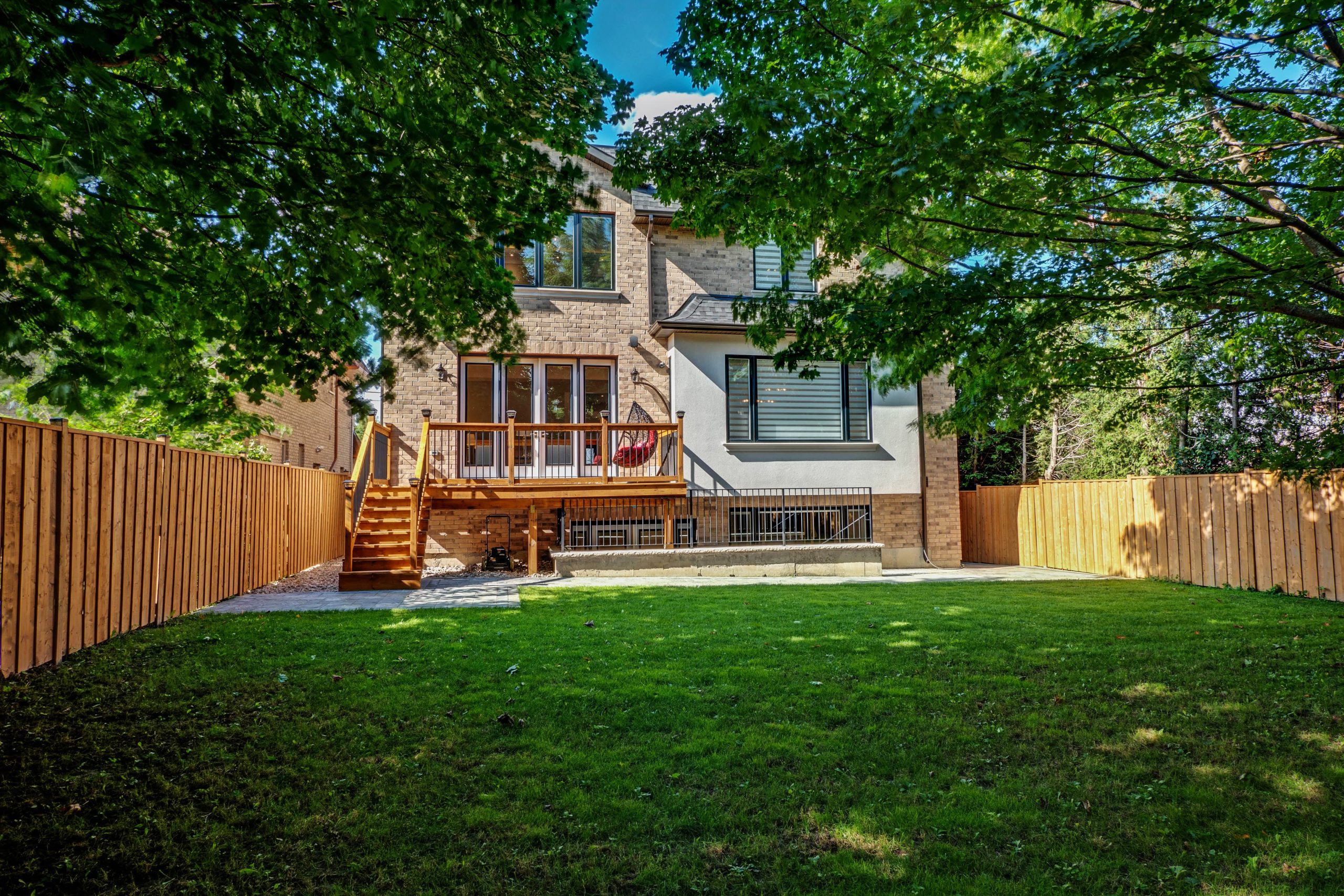 Rear of a two-storey brick home with a new elevated cedar-toned deck, fresh sod, and wood privacy fence on both sides