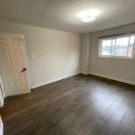 Completed flooring installation in an empty bedroom, dark gray-brown wide planks with white baseboards