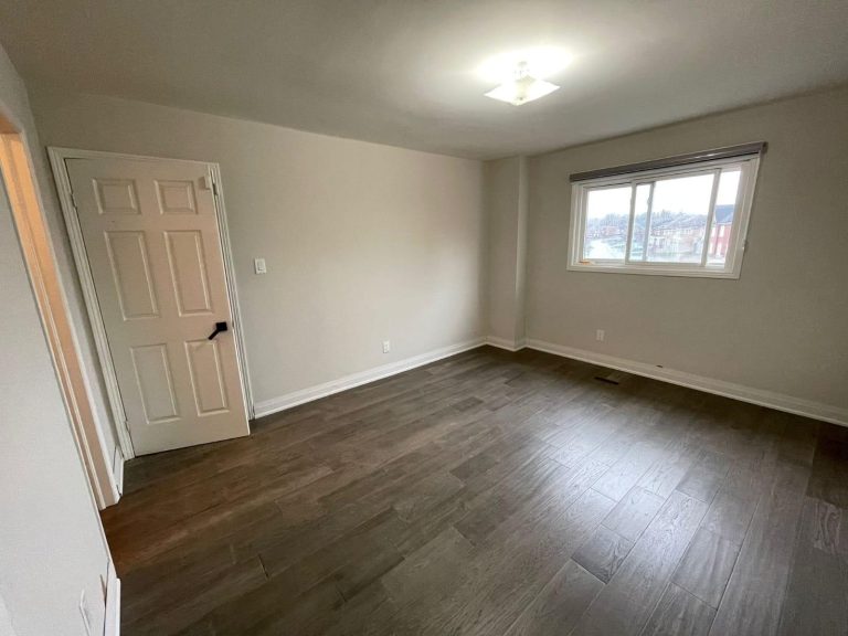 Completed flooring installation in an empty bedroom, dark gray-brown wide planks with white baseboards