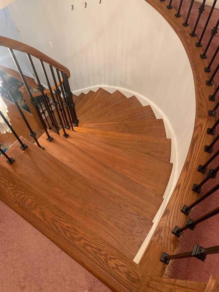 Top-down view of a curved winder staircase with stained oak treads, oak handrail and black square-collar balusters