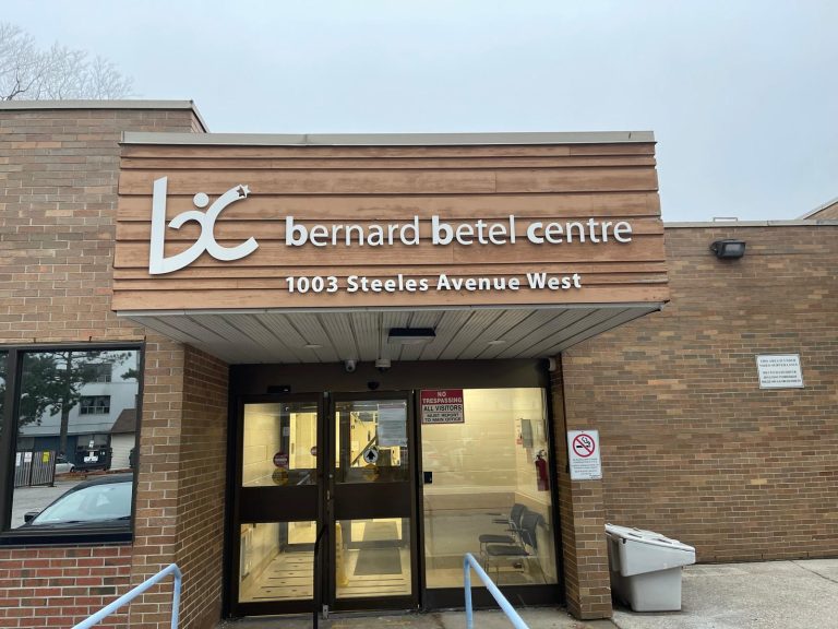 Main entrance of the Bernard Betel Centre in Toronto with wood-clad signage canopy over automatic glass doors